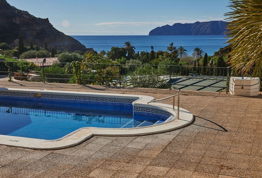 une piscine entourée d' ombrelles de paille et d' une maison blanche