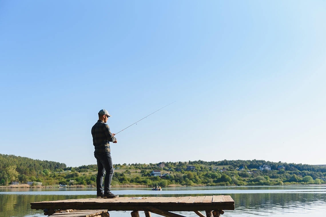 un hombre de pie en un muelle con una caña de pescar