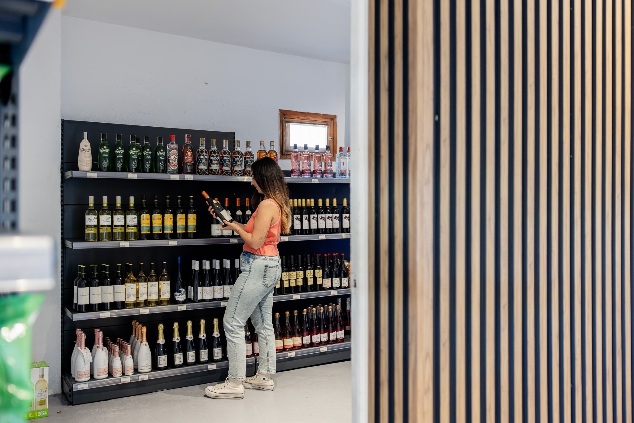 Een vrouw staat in een winkel en bekijkt flessen wijn en sterke drank die op schappen staan.