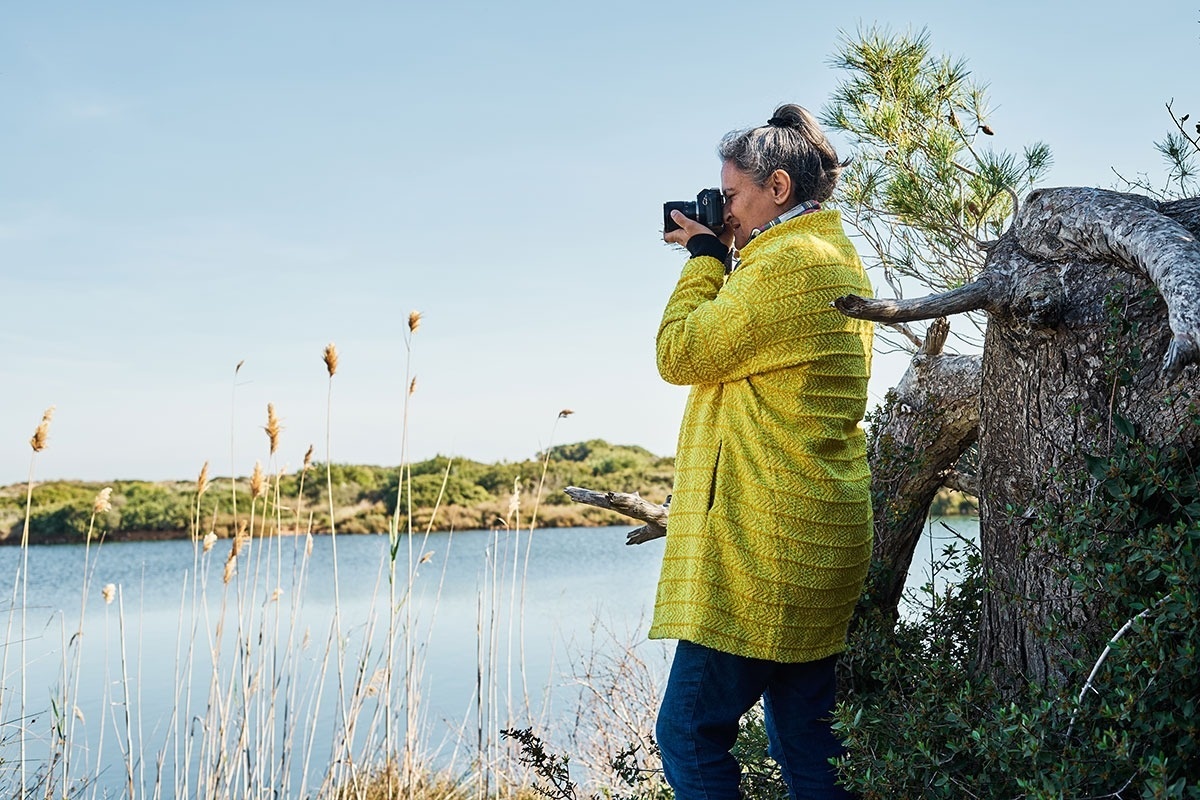 Eine Frau in einem gelben Mantel fotografiert einen See