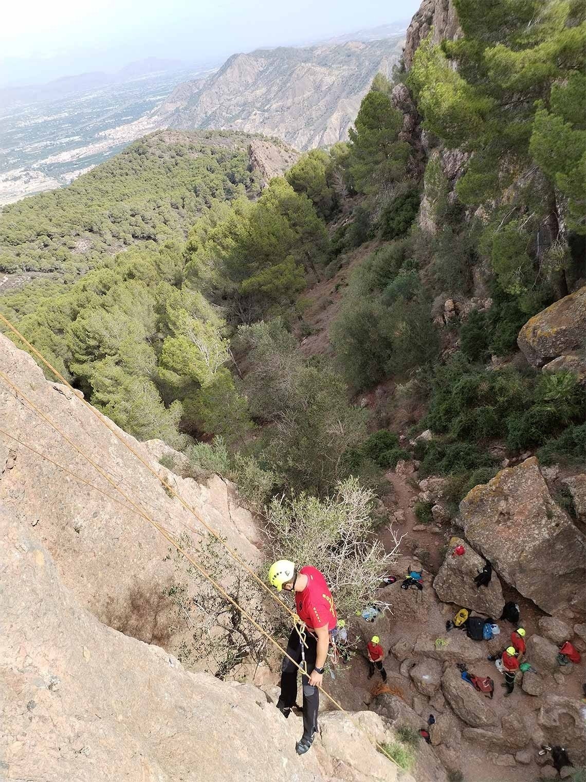 a man wearing a red shirt that says ' a ' on it climbs a rocky cliff