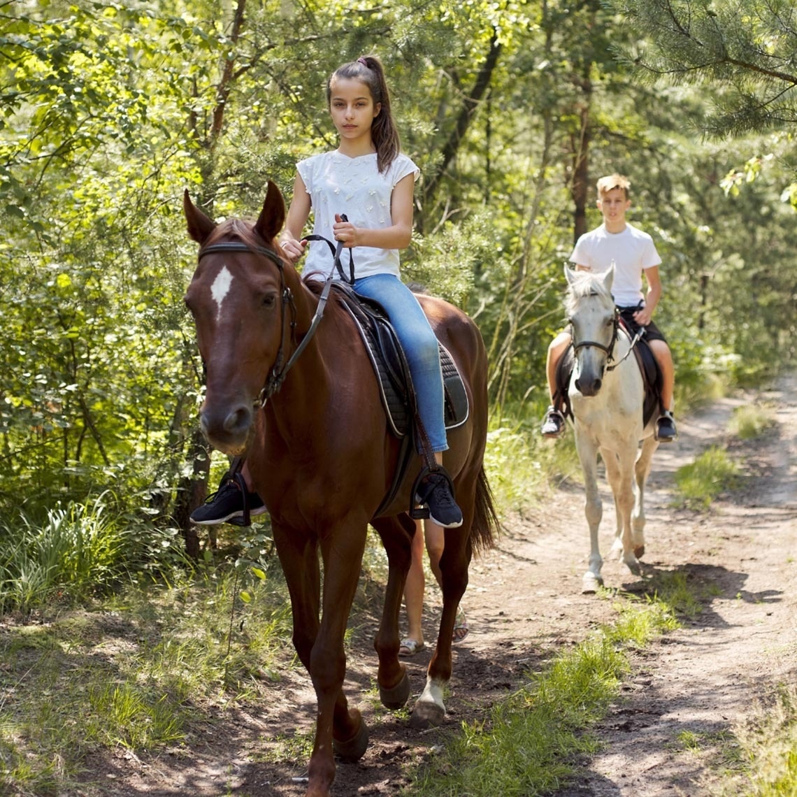 un niño y una niña montan a caballo por un camino de tierra