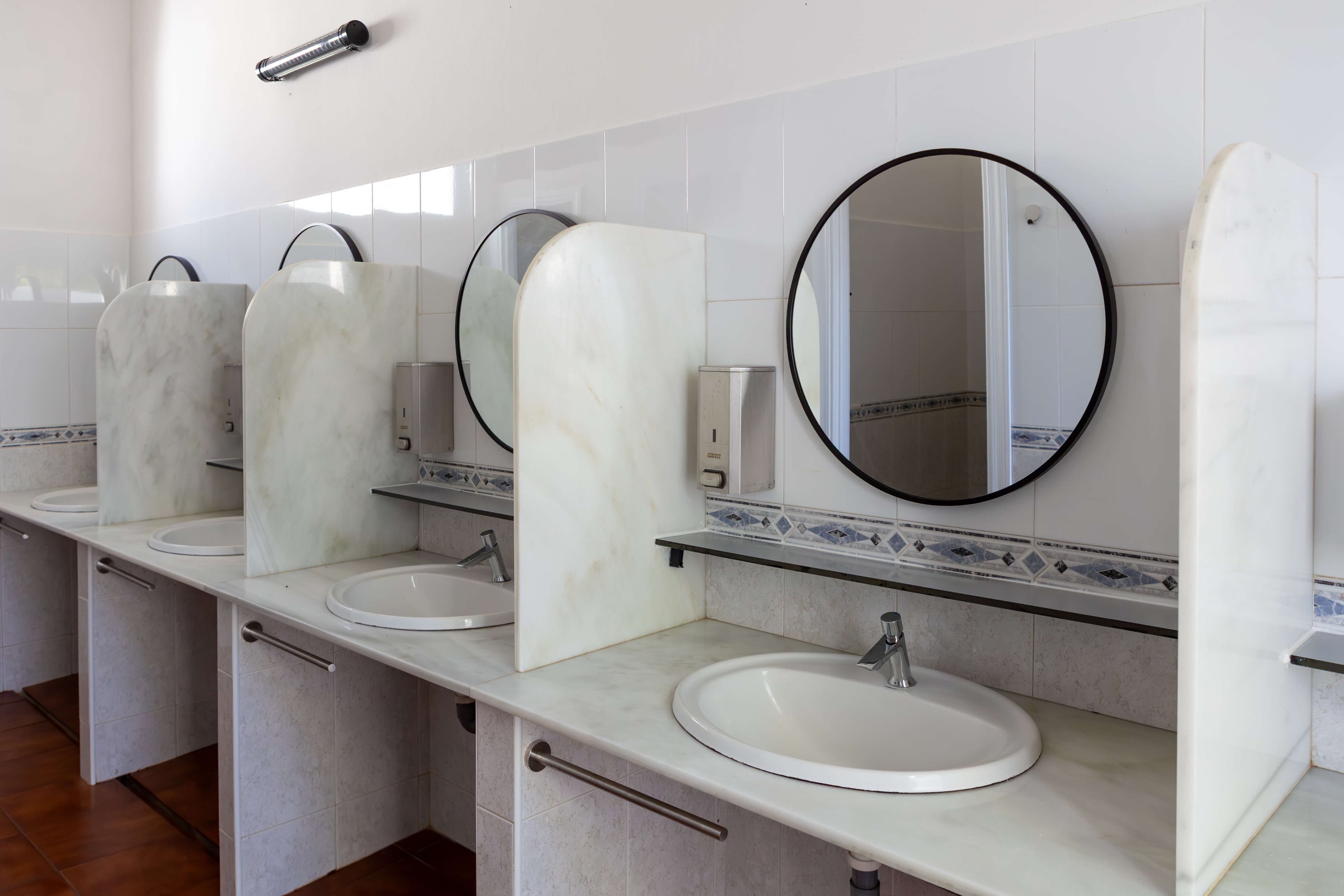 Lavabos moderns d'hotel amb miralls rodons i separadors de marbre, disseny Taiga: Corporativa.