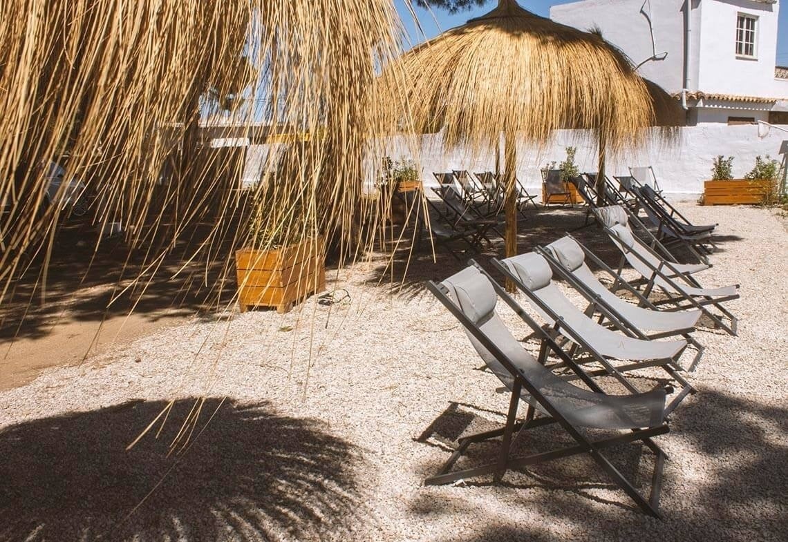 een rij ligstoelen onder een strooien paraplu