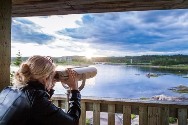 a woman looking through a telescope at a lake