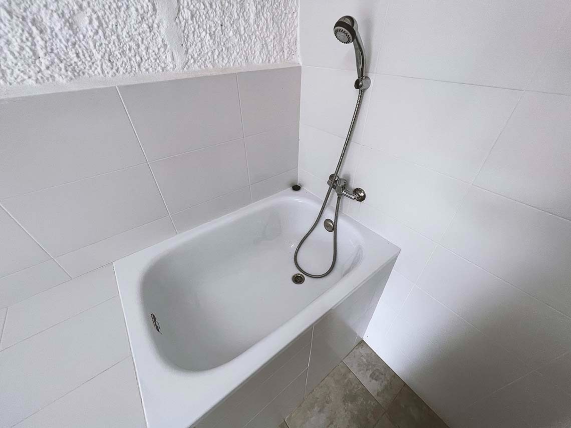 een witte badkuip met een douchekop aan de muur