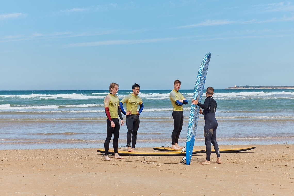 un grupo de surfistas se paran en la playa y uno de ellos sostiene una tabla de surf