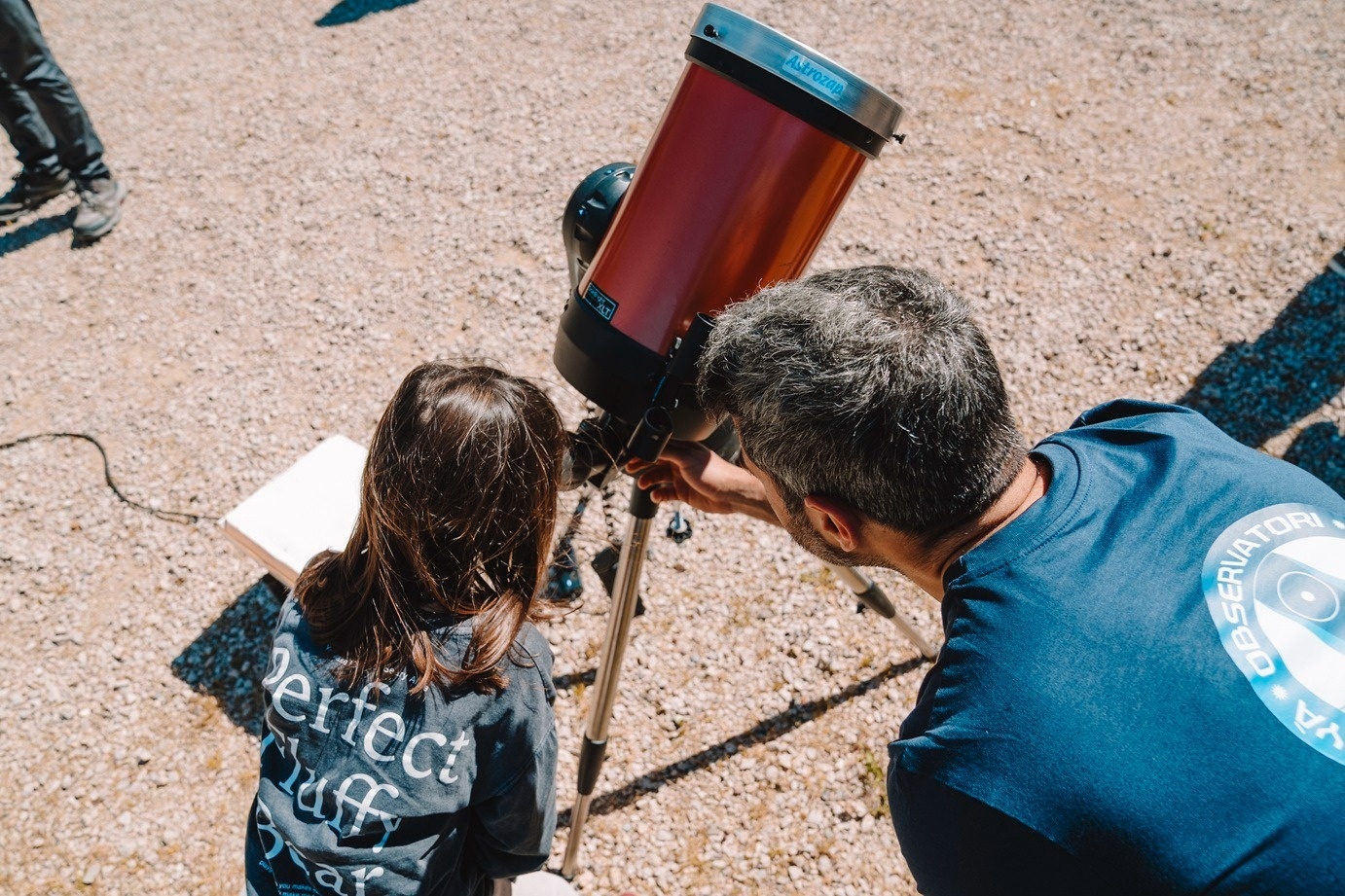 Adulto y niña en observación astronómica con telescopio al aire libre.