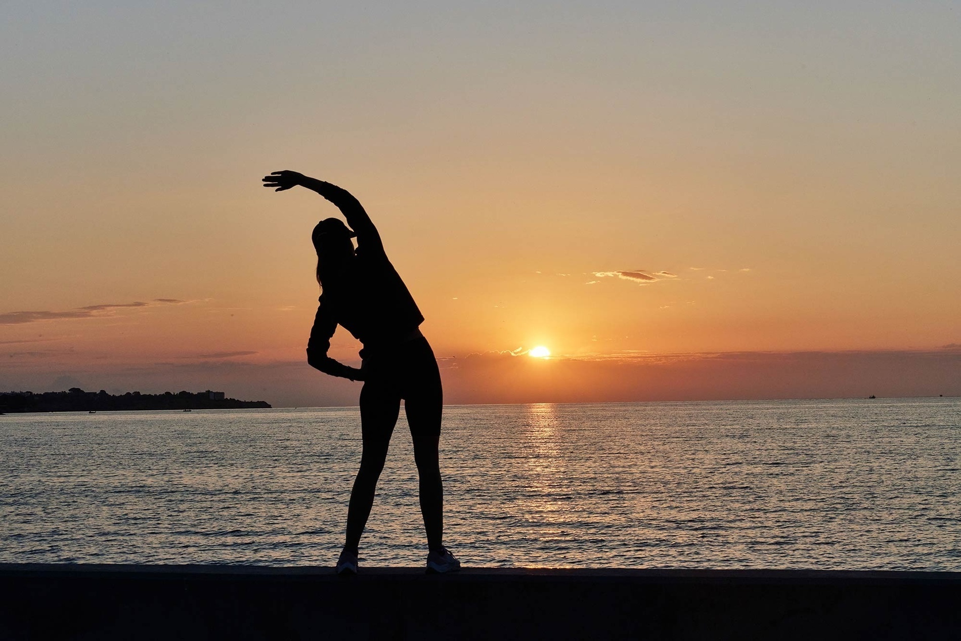 a silhouette of a woman stretching on the beach at sunset