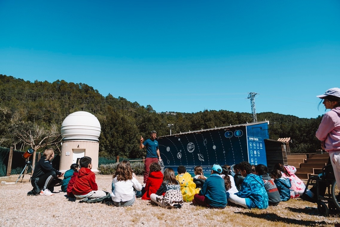 Niños aprenden sobre planetas y estrellas con guía en observatorio al aire libre y telescopio.