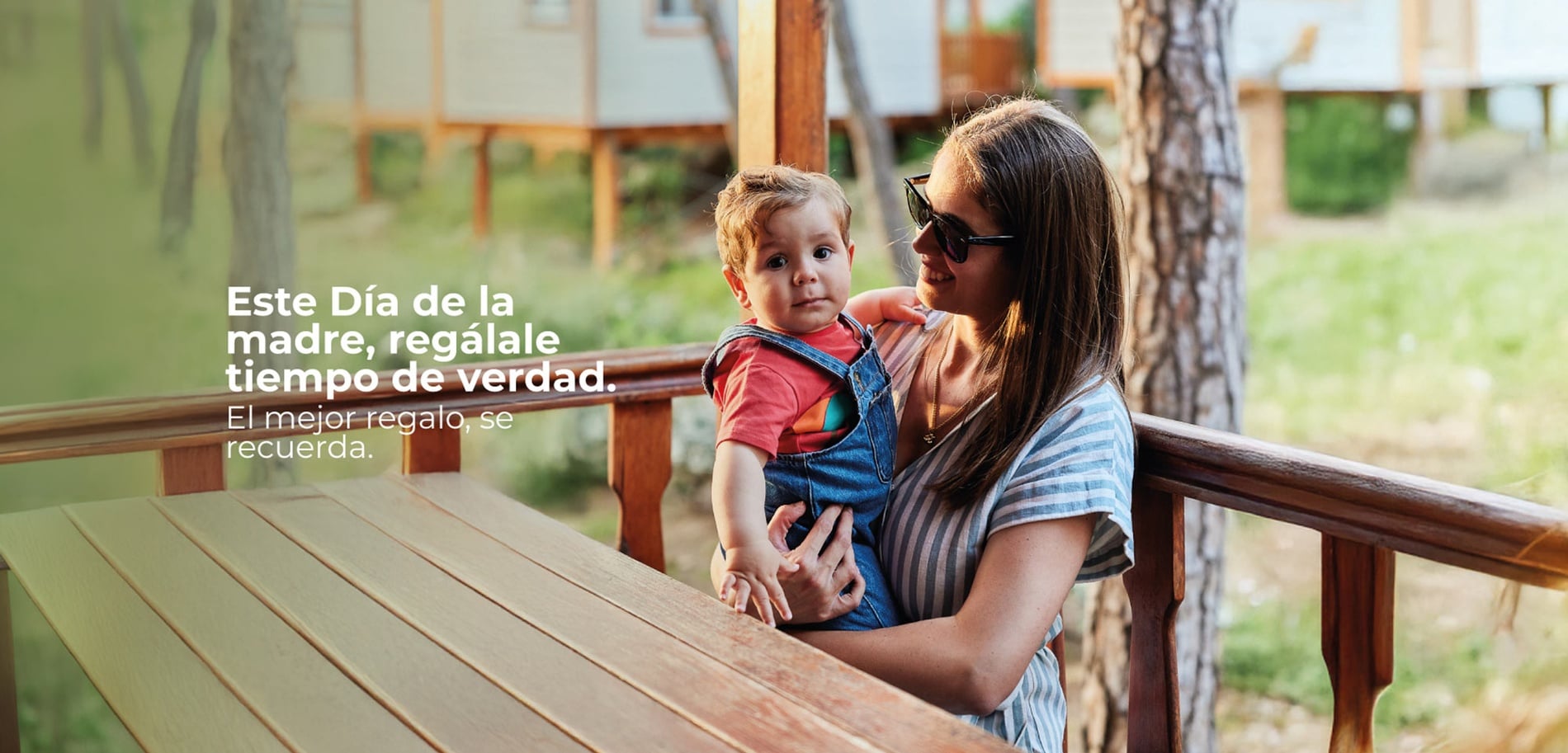 Una familia feliz disfruta de un momento de interacción y alegría con su hijo pequeño en la terraza de una cabaña de madera, rodeada de un entorno natural y boscoso.