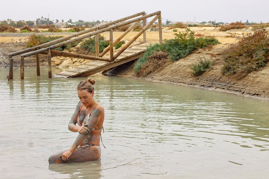 a woman in a bikini is kneeling in the water covered in mud
