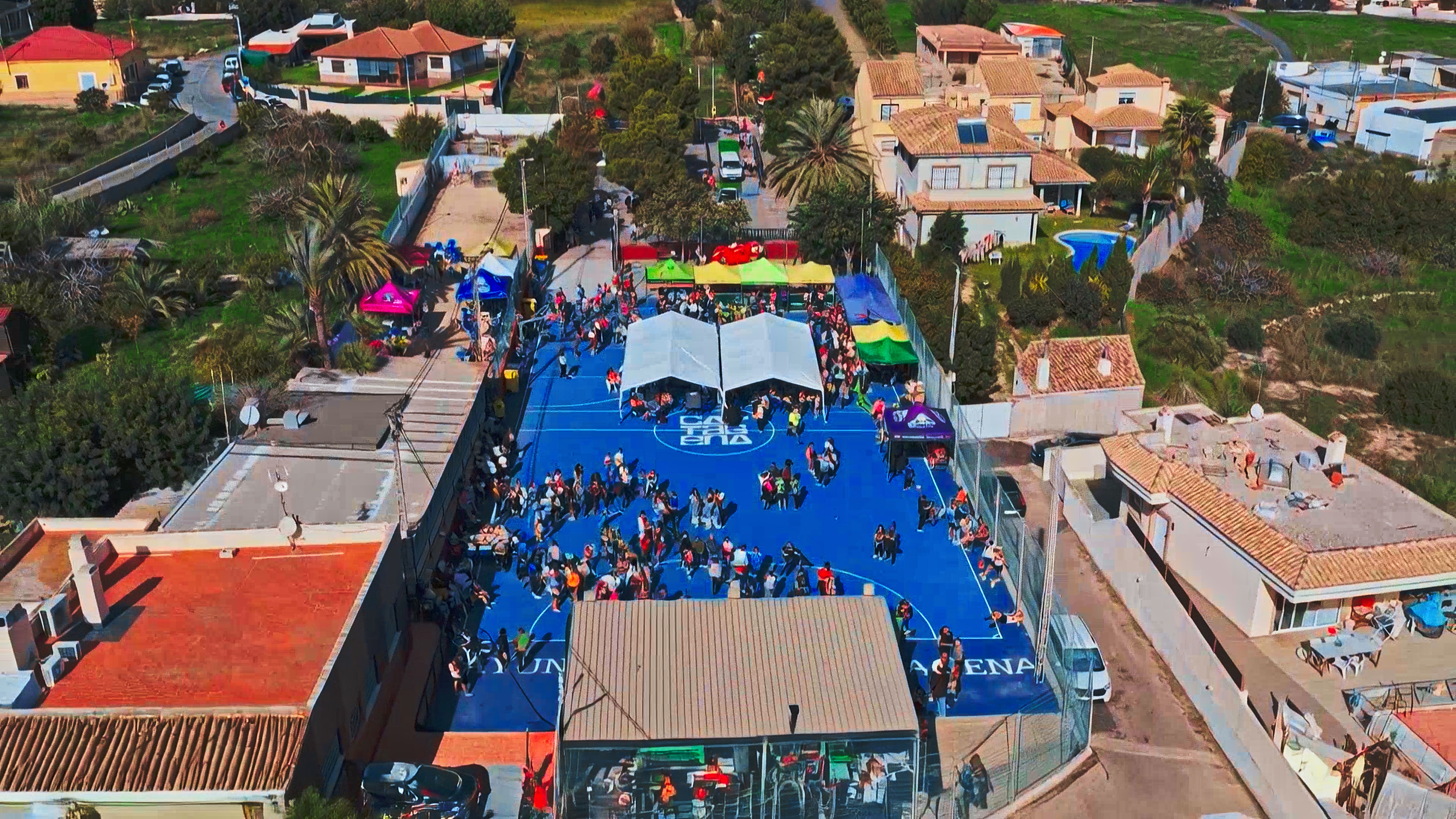 Outdoor event with colorful tents and many people on a blue court at a Taiga: Corporativa in Spain.