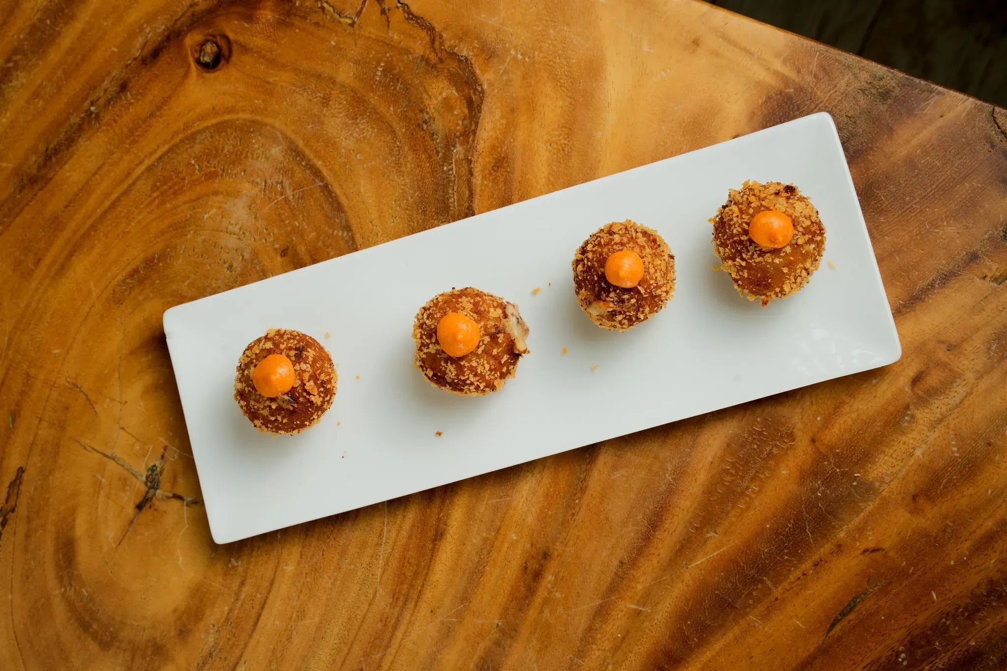 four fried food balls on a white plate on a wooden table