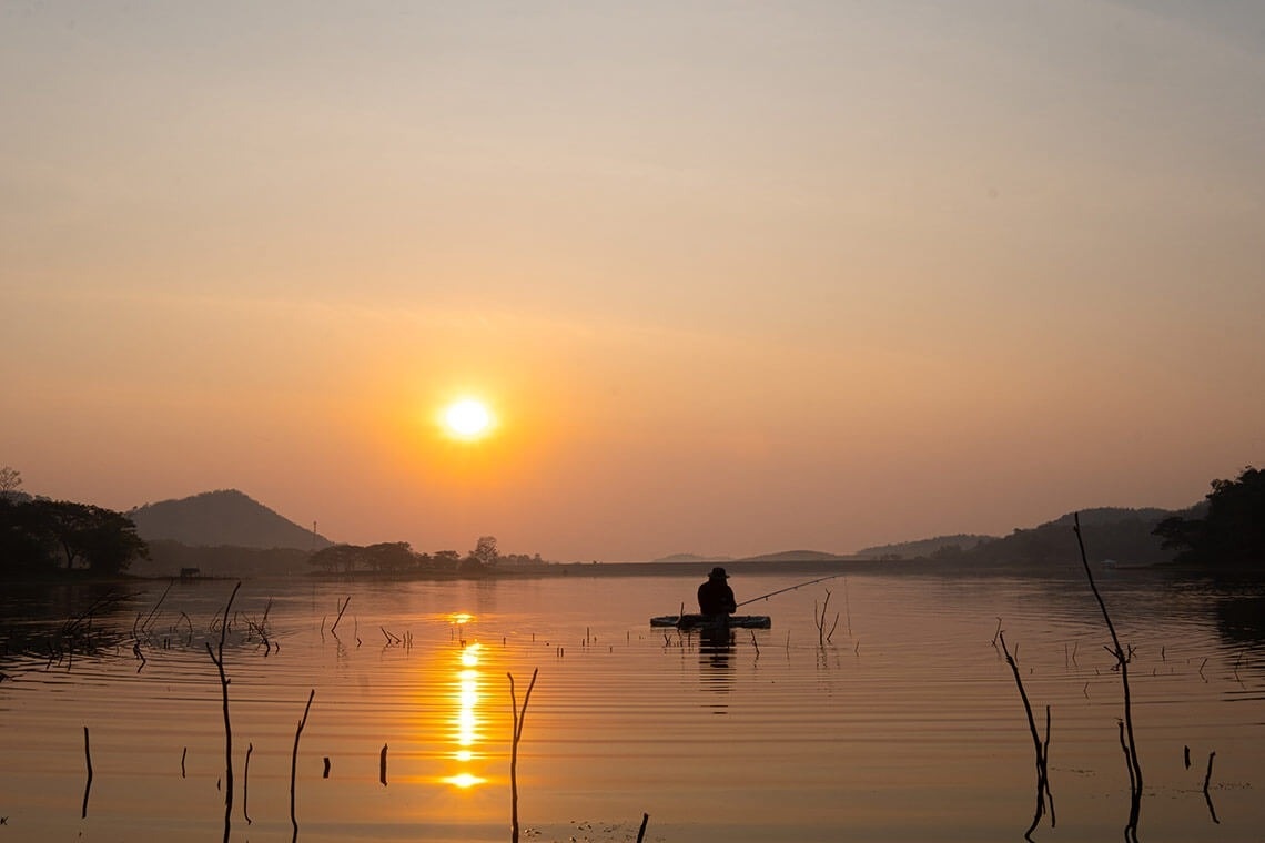 un hombre pesca en un bote al atardecer