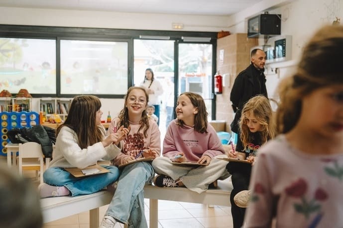 Niñas alegres dibujan y ríen en un espacio luminoso, perfecto para actividades infantiles del hotel.