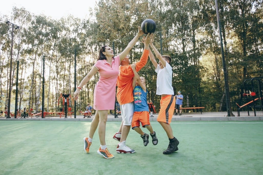 una madre y sus hijos juegan a baloncesto en un parque