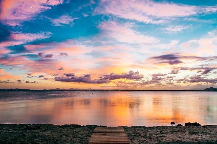 un muelle de madera conduce a una playa al atardecer