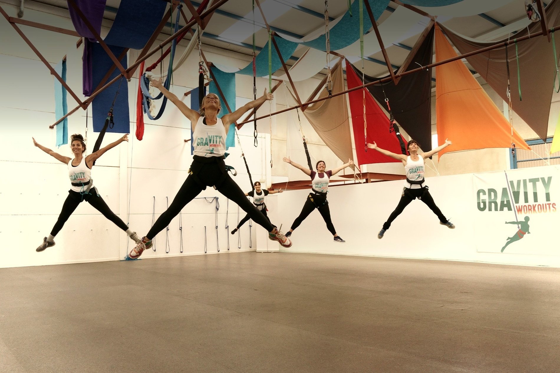 een groep vrouwen springt in de lucht in een gym met een banner voor gravity workouts