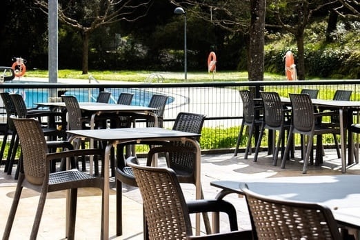 Terraza exterior de hotel con mesas y sillas junto a la piscina.
