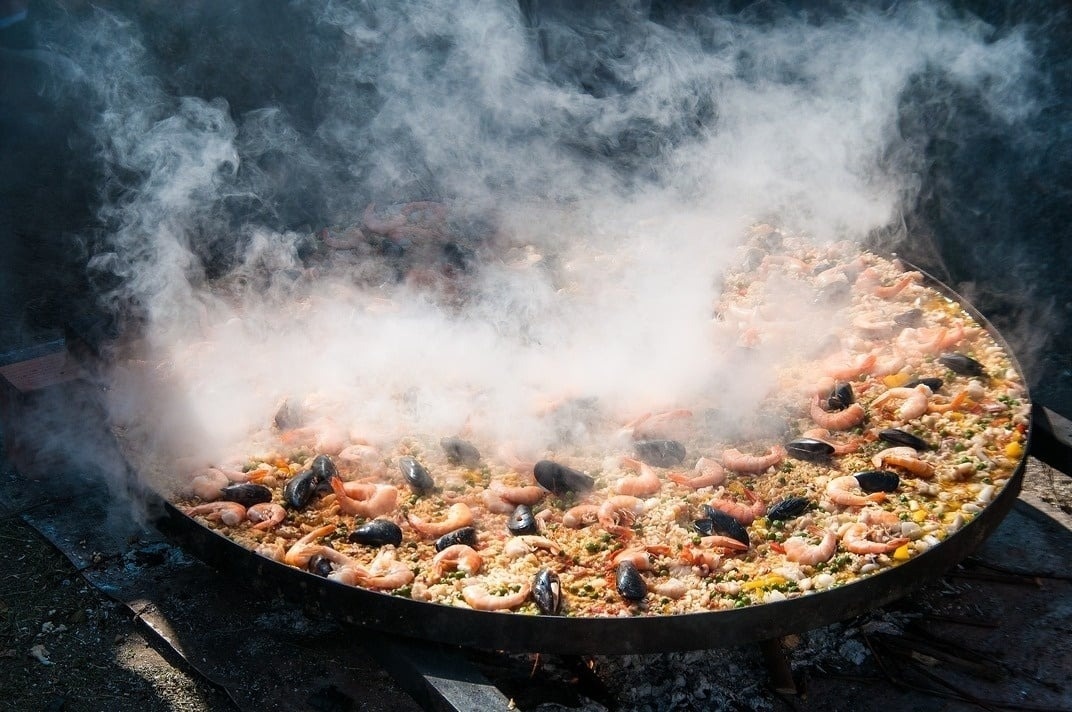 a large pan filled with shrimp mussels and rice with smoke coming out of it