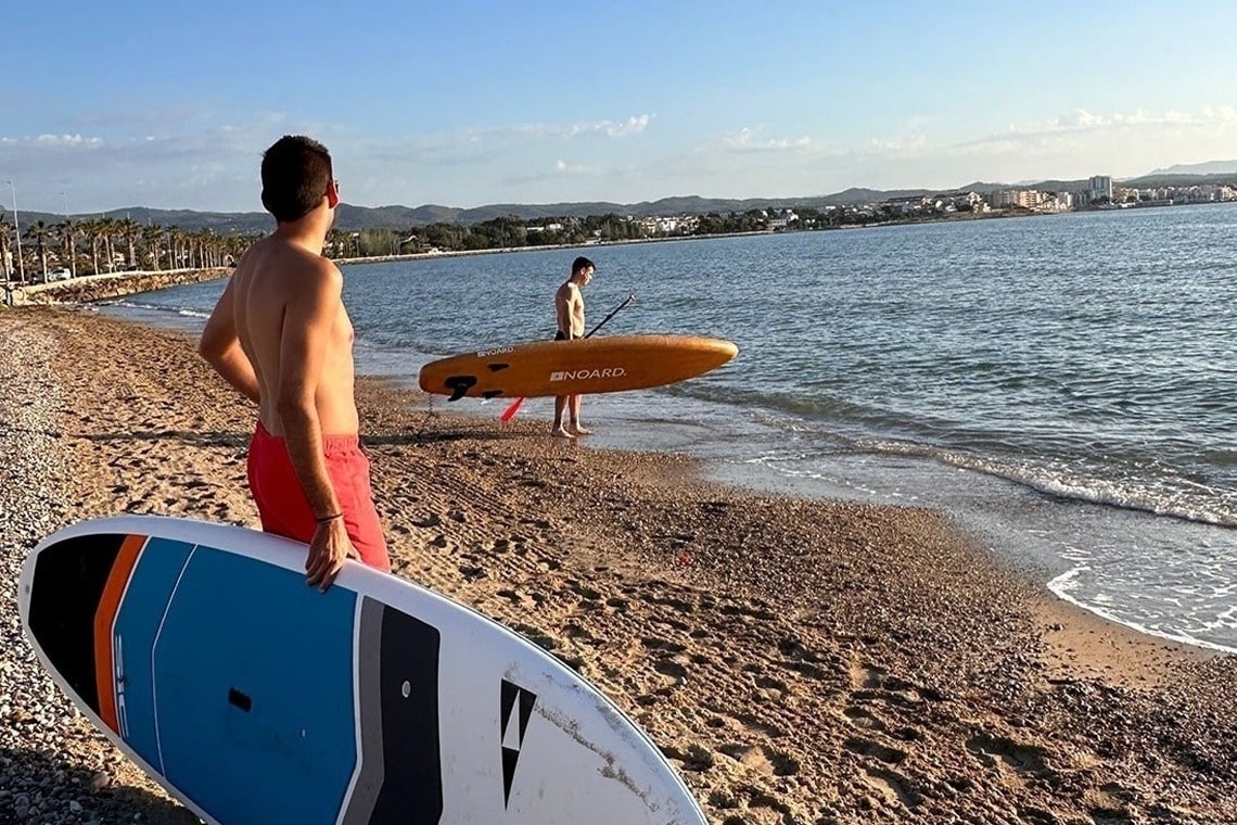 Varias personas disfrutan del kayak y la natación en aguas turquesas y claras junto a imponentes acantilados rocosos.