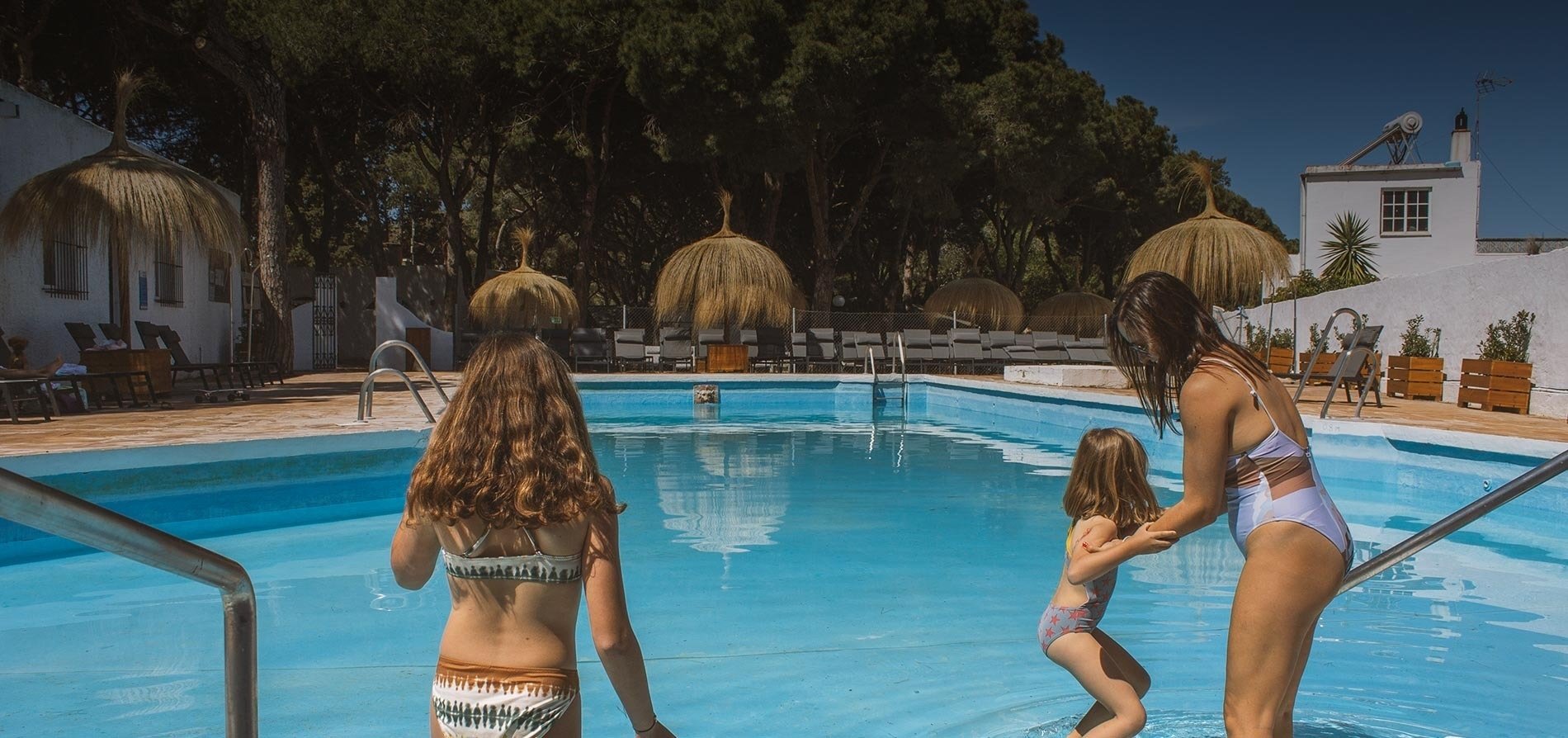 een vrouw en twee meisjes in bikini staan in een zwembad