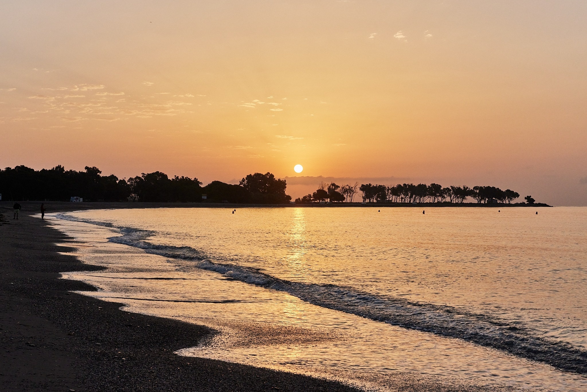 de zon gaat onder boven de oceaan met bomen op de achtergrond