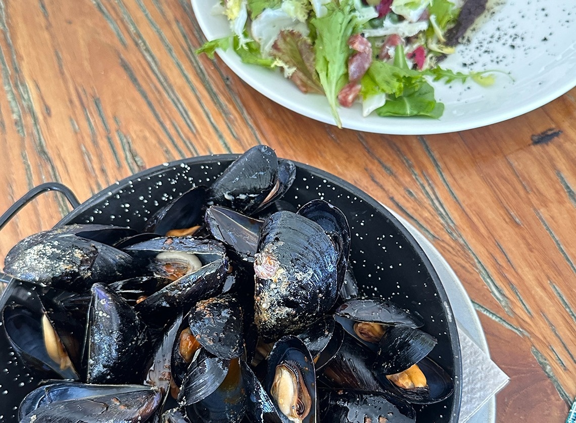 a bowl of mussels next to a plate of salad