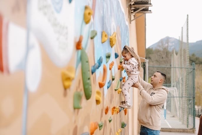 Muro de escalada infantil en hotel. Padre y niña jugando, diversión familiar.
