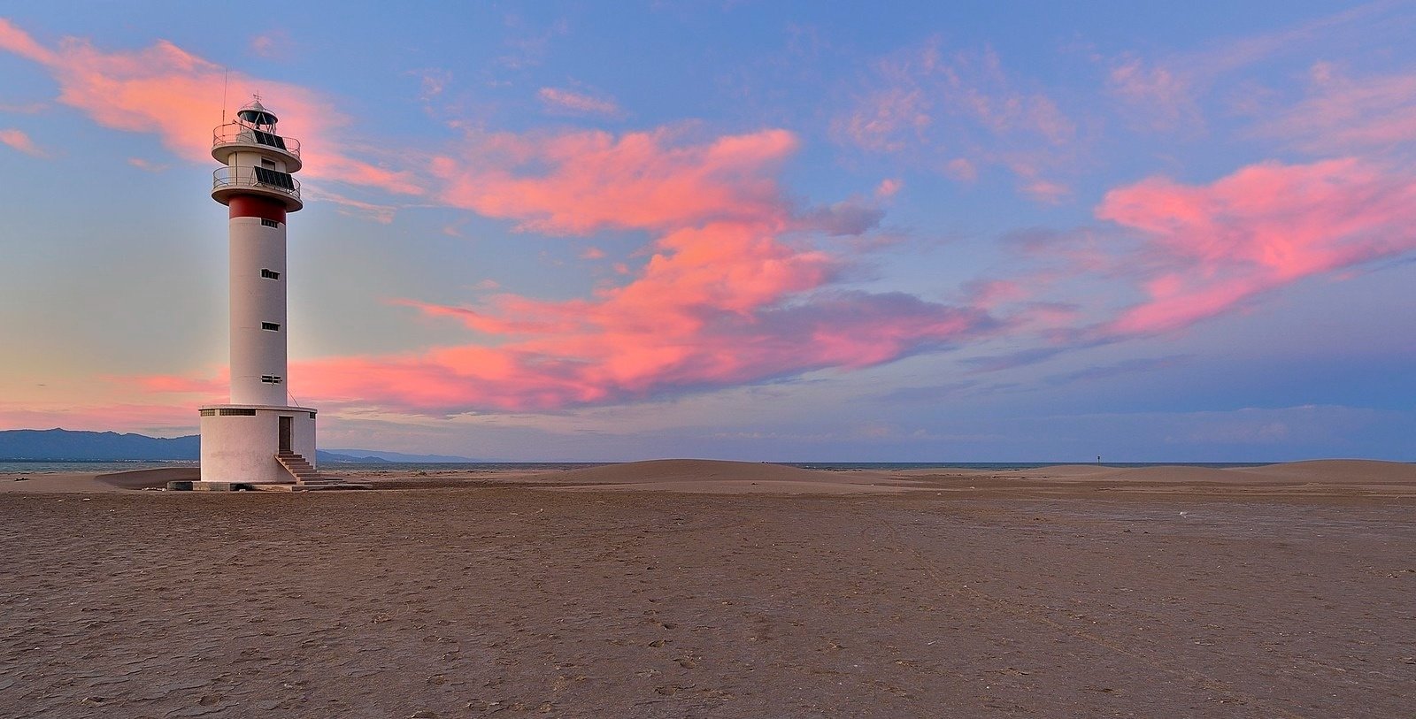 a lighthouse in the middle of a desert with pink clouds in the sky