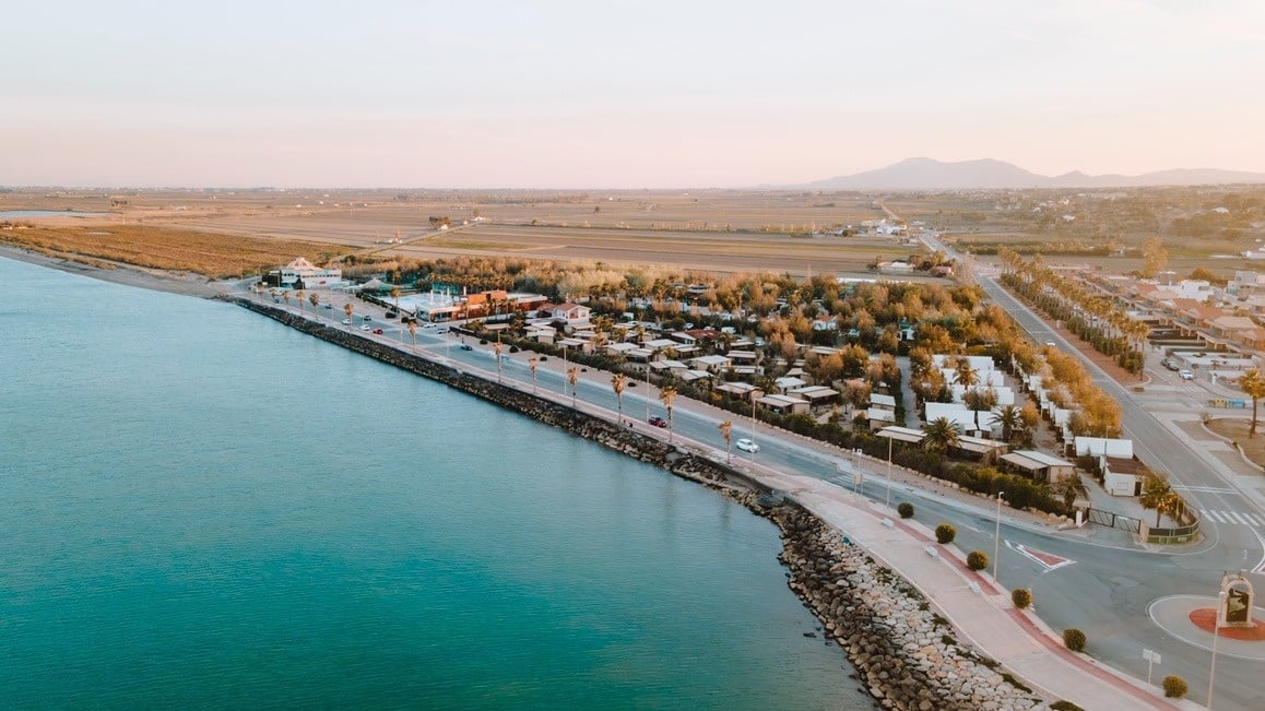 Vista aérea de resort costero al atardecer, con palmeras, carretera y el mar turquesa.