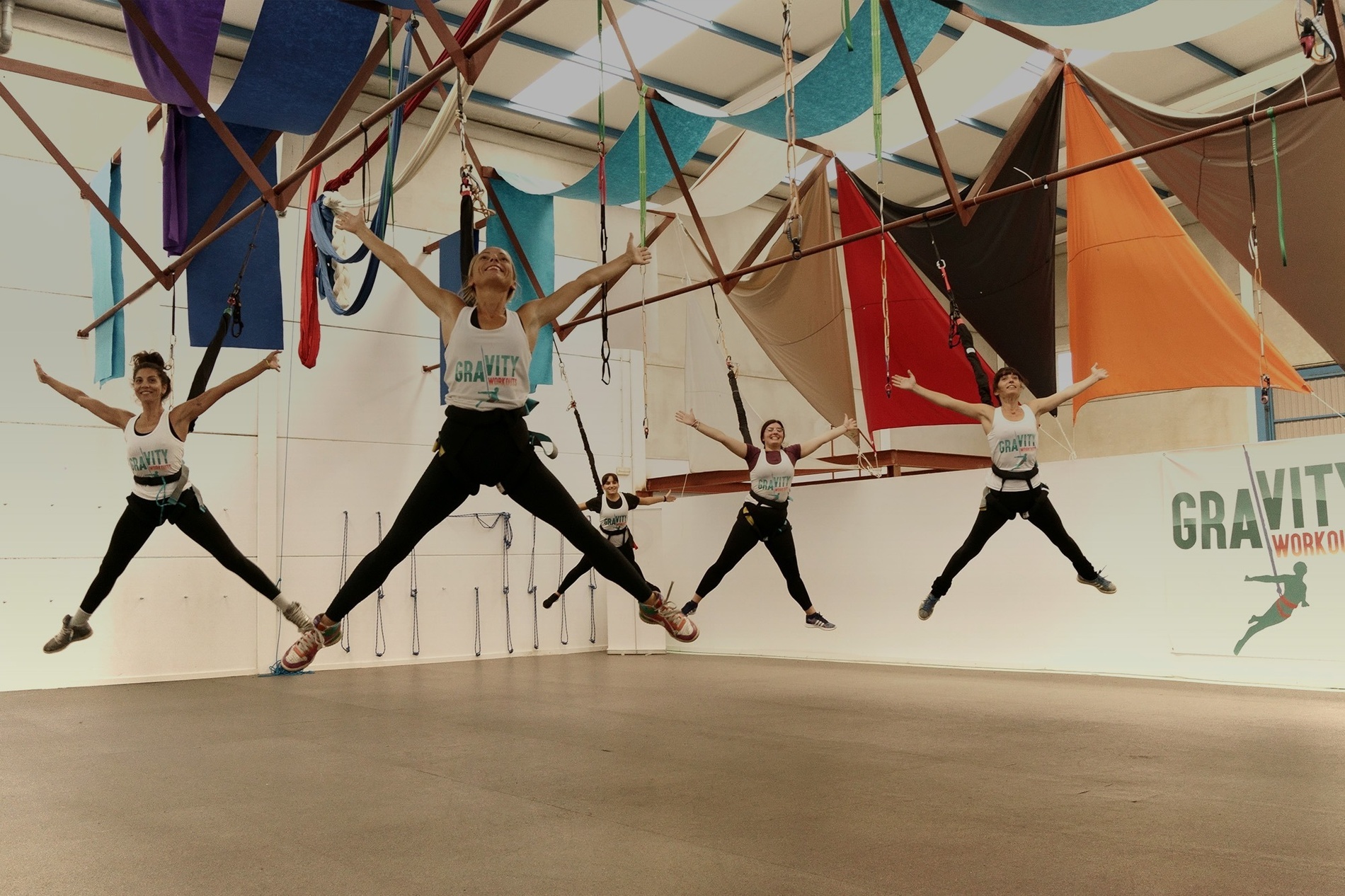 een groep vrouwen springt in de lucht in een gym met een banner voor gravity workouts