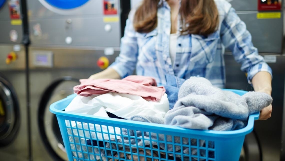 een vrouw draagt een blauwe wasmand gevuld met kleding