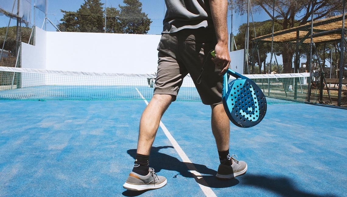 een man houdt een padelracket vast terwijl hij op een tennisbaan loopt