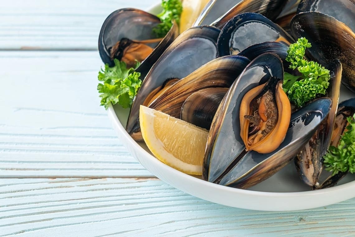 eine weiße Schüssel mit Muscheln und einer Limettenscheibe