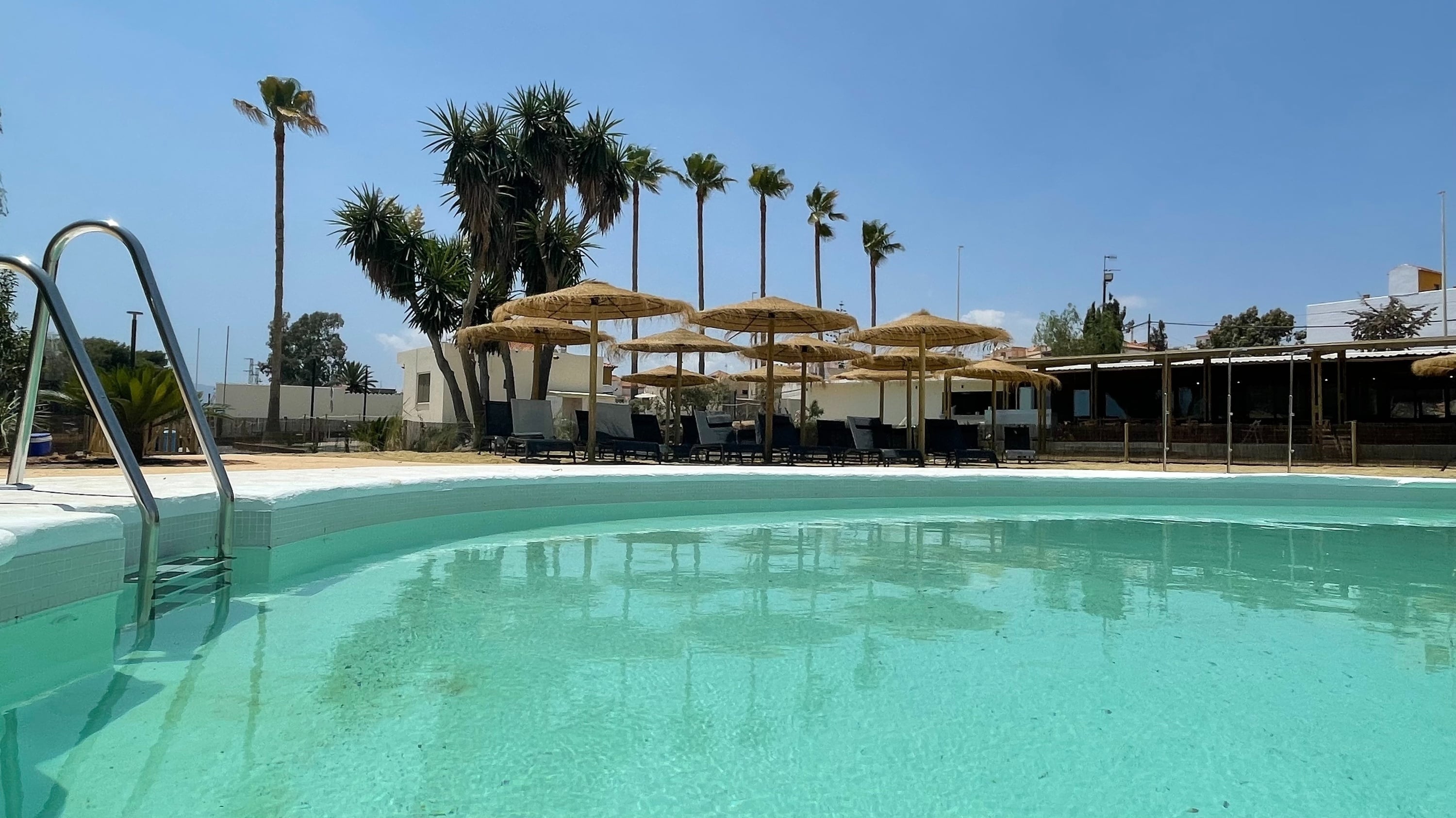 una piscina rodeada de palmeras y un edificio en el fondo