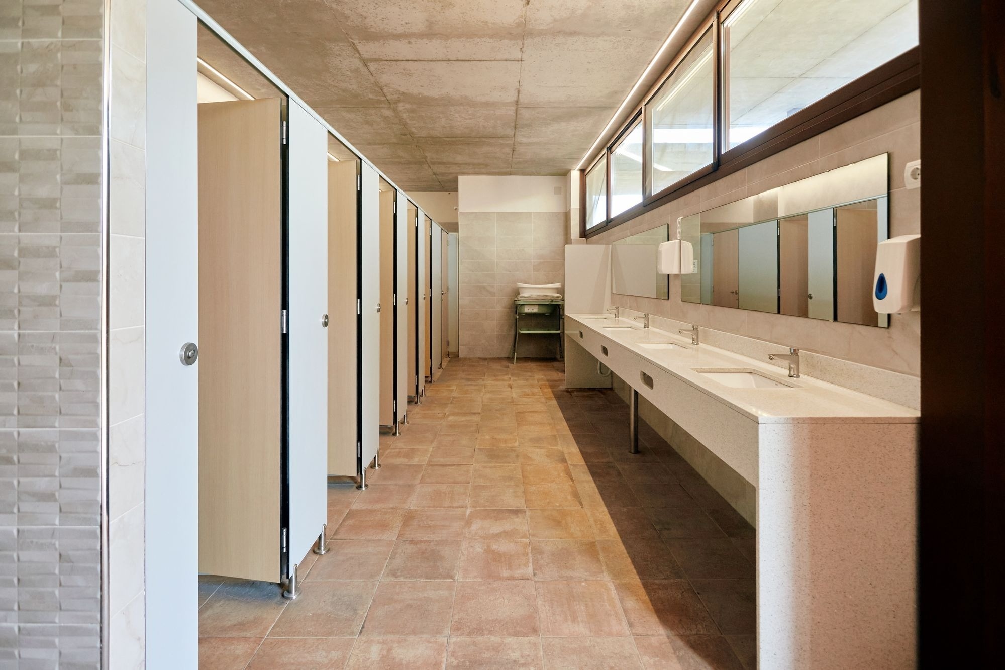 een lange gang in een badkamer met veel wastafels en spiegels