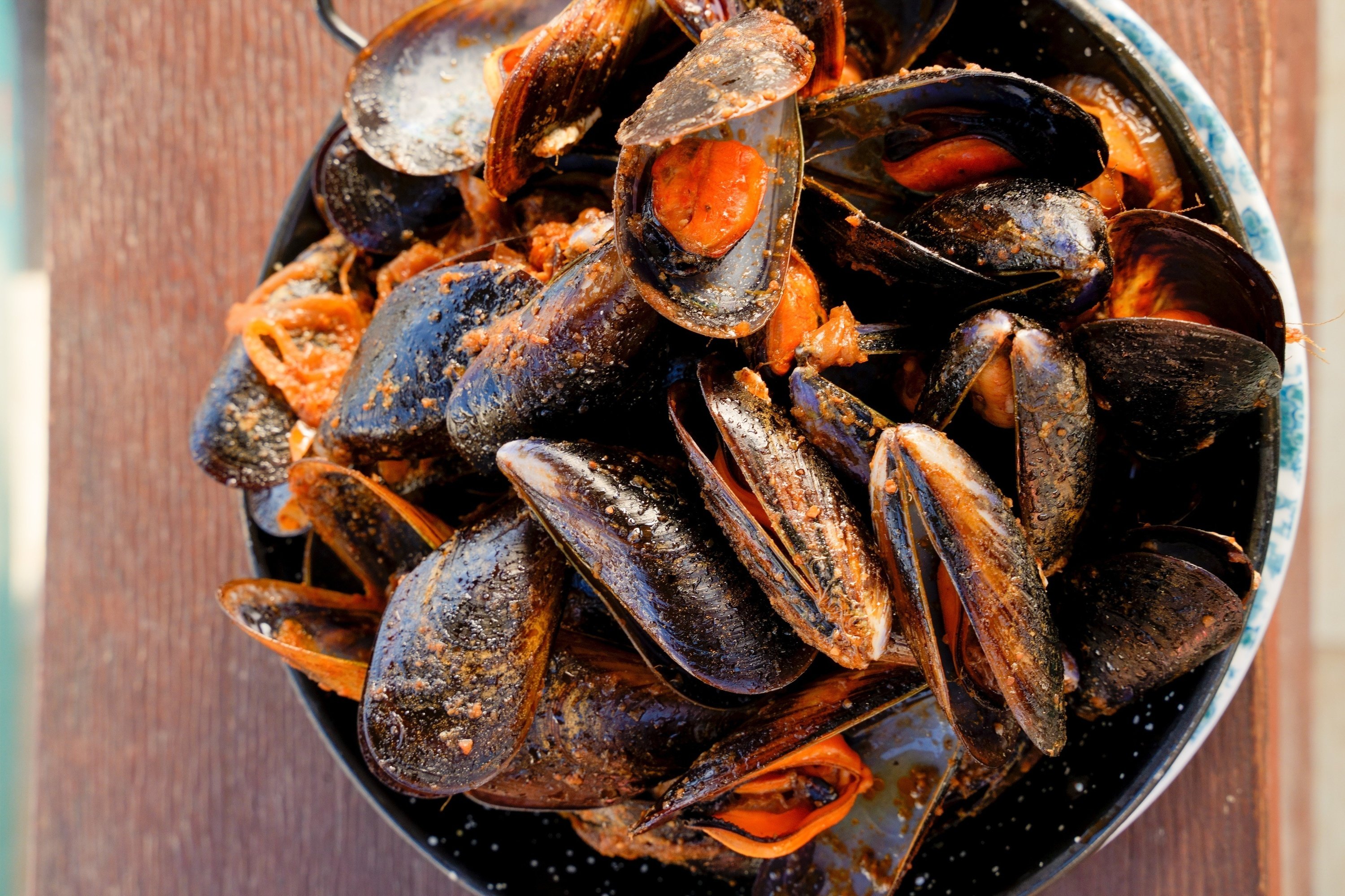 a bowl of mussels covered in sauce on a wooden table