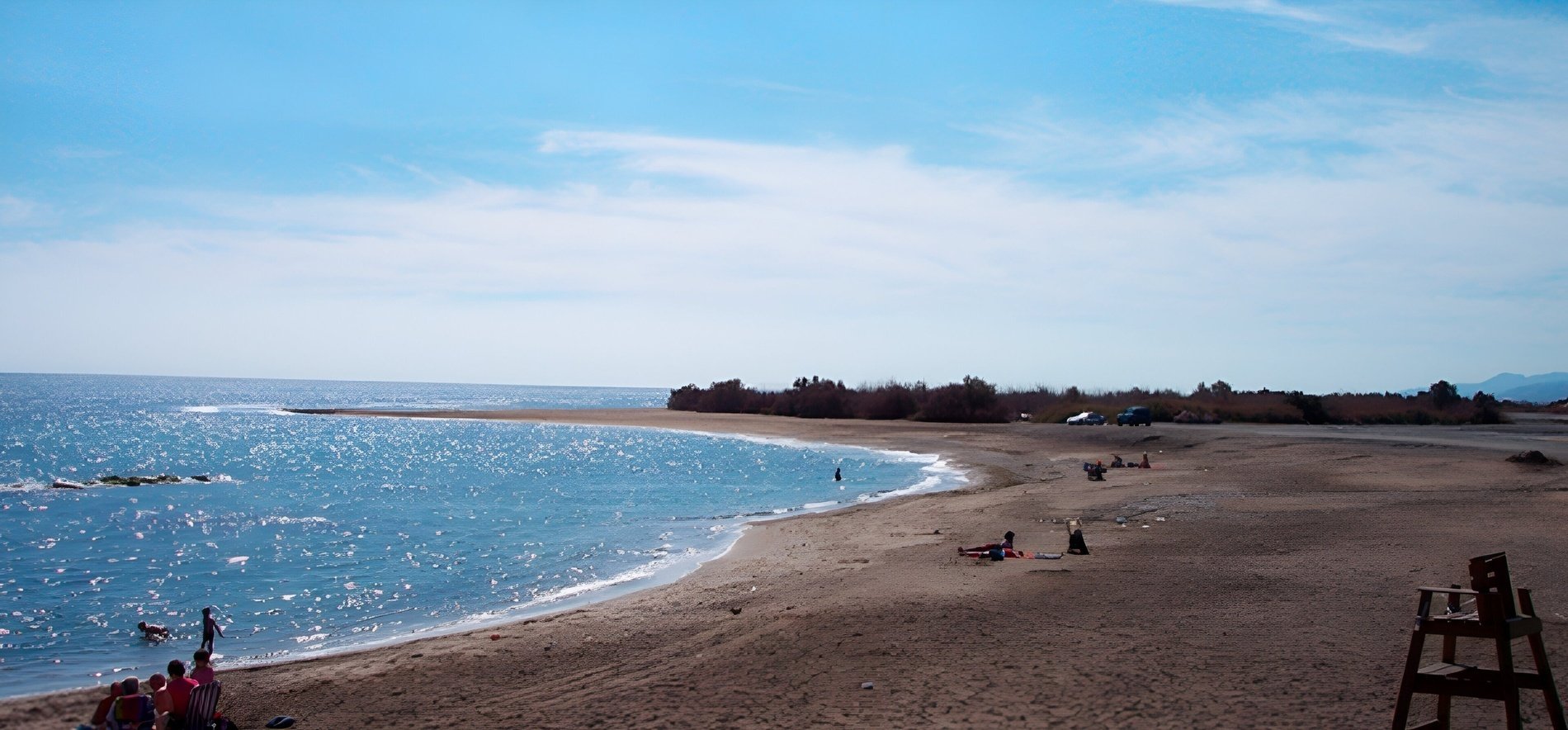 een groep mensen staat op een strand met een reddingsstoel in de voorgrond