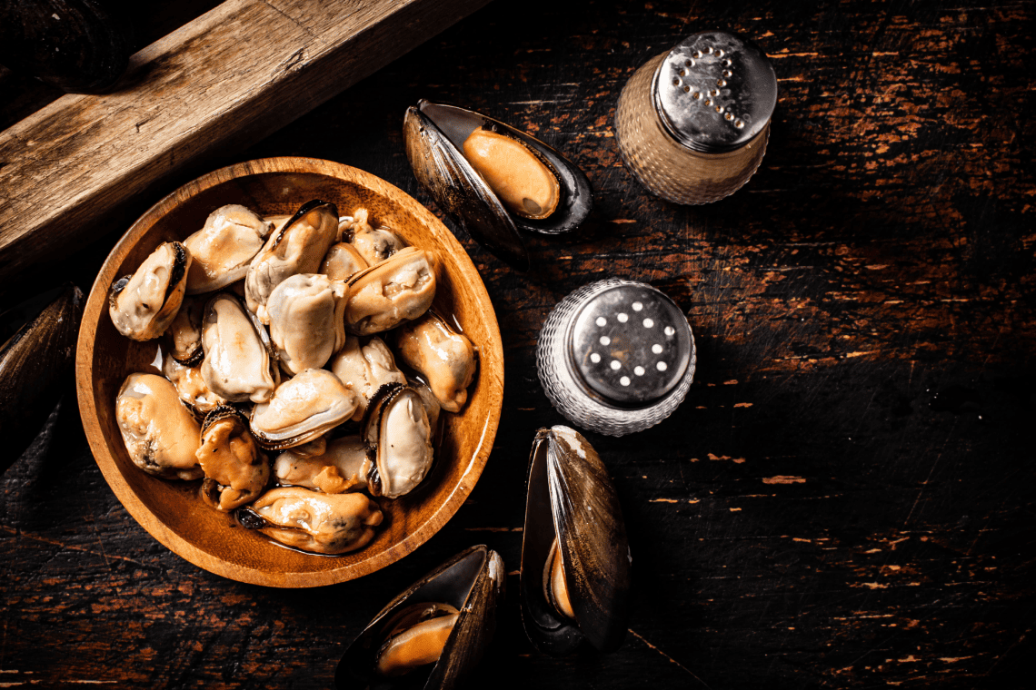 a bowl of mussels sits on a wooden table next to salt and pepper shakers