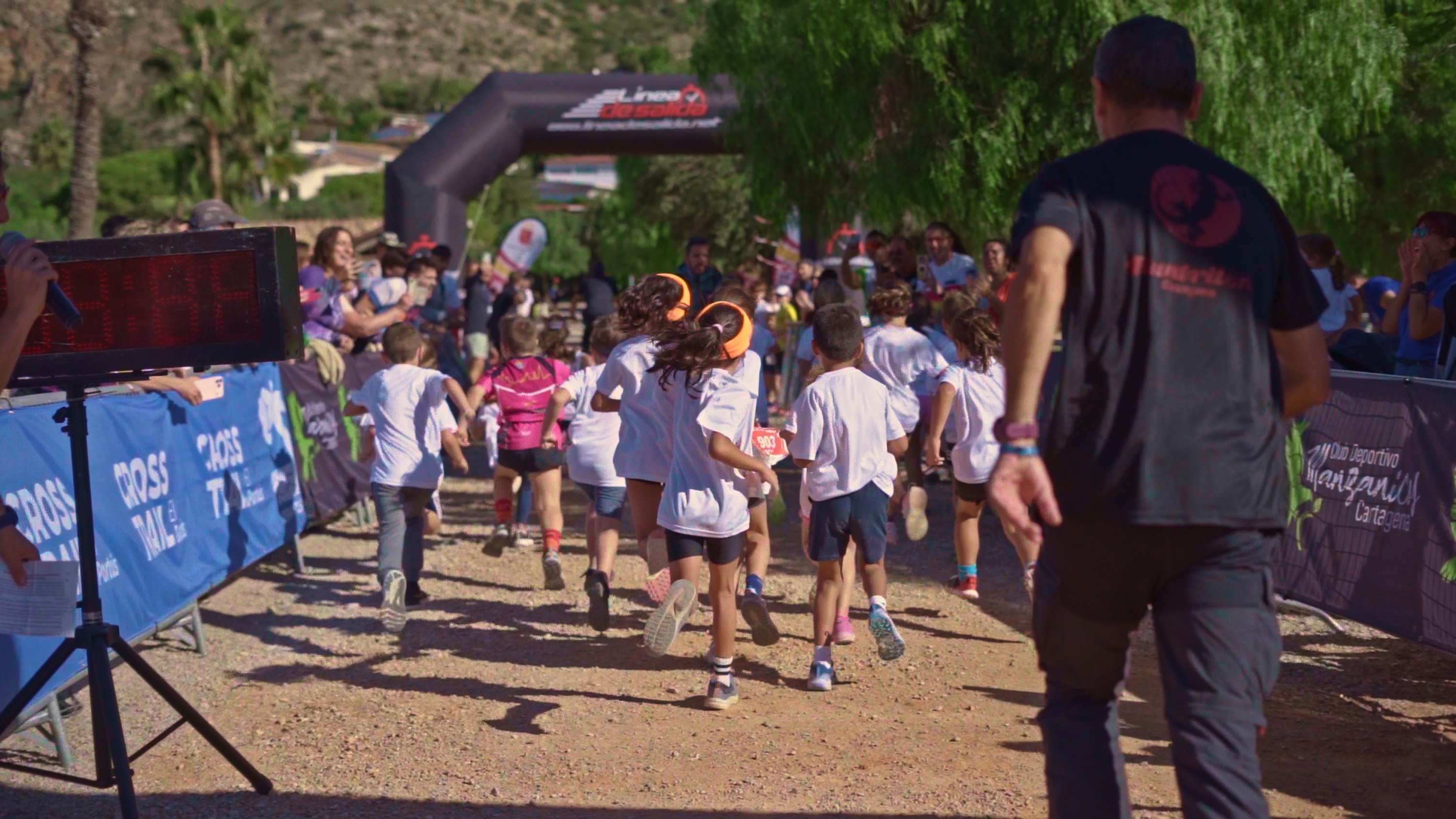 Children running a race at a Taiga: Corporativa event, with spectators and a finish line arch in the background.