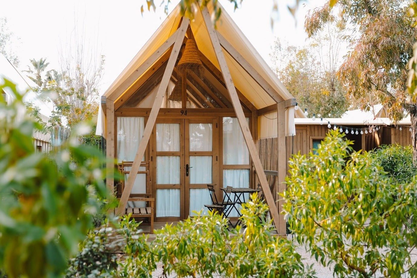 Luxury glamping tent with wooden frame, outdoor seating, and lush green surroundings at a serene resort.