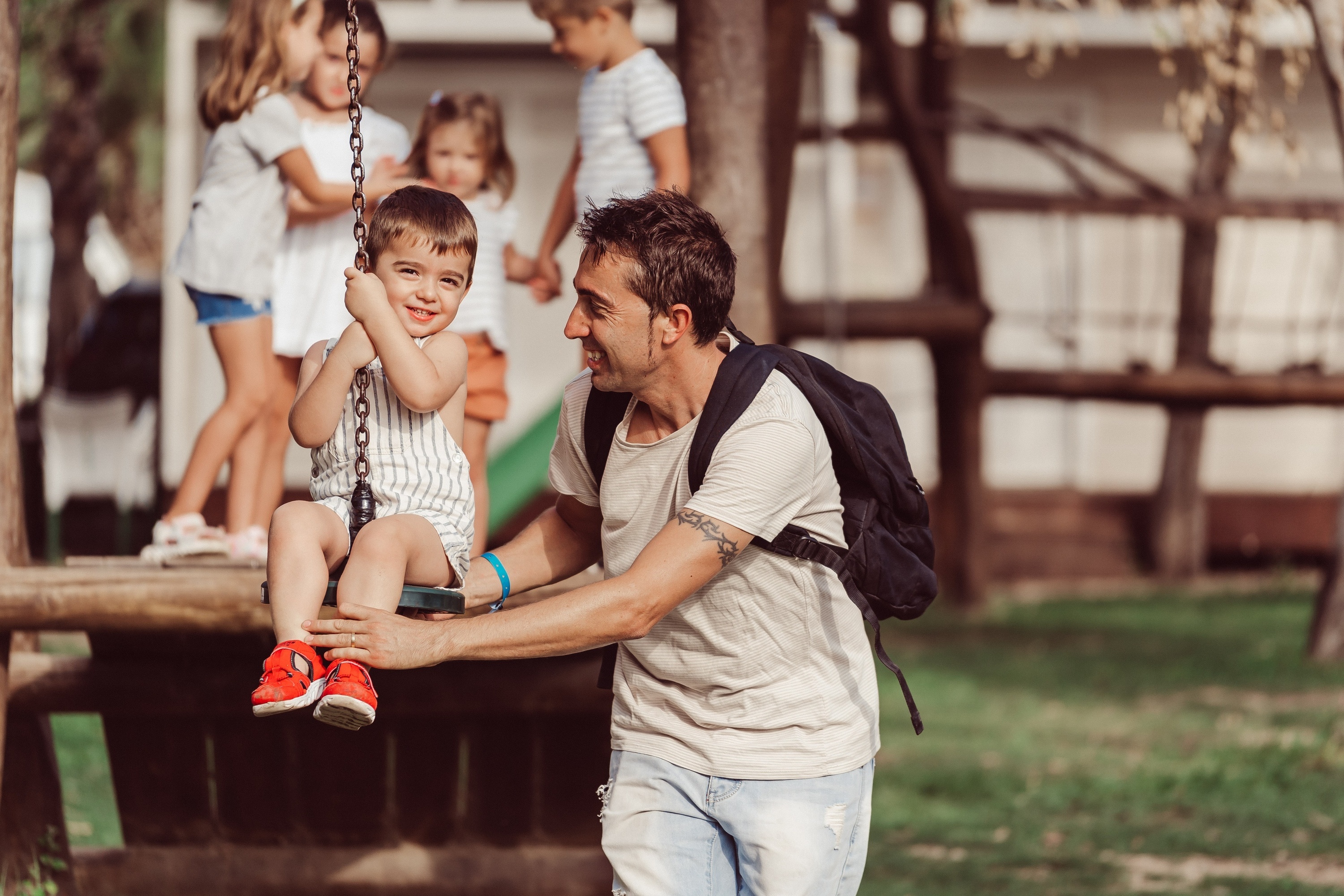 a man with a backpack holds a child on a swing