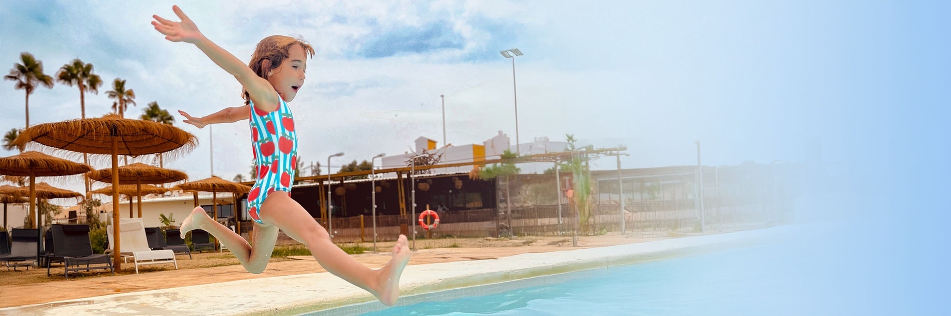 una niña salta en una piscina con un restaurante en el fondo