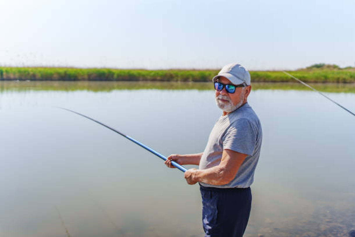 een oudere man houdt een hengel vast en vist op een meer .
