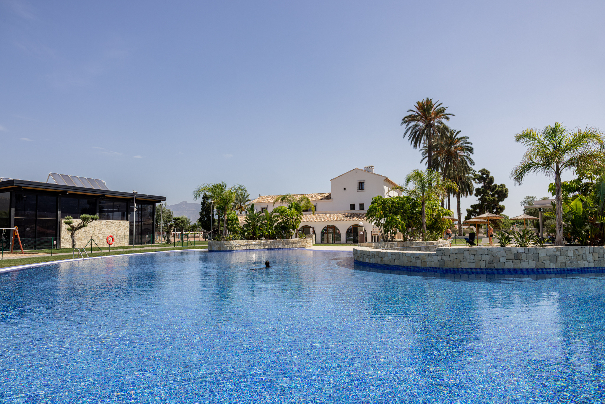 Piscina de hotel Taiga: Corporativa de azulejos azules, rodeada de palmeras y edificios de estilo mediterráneo.