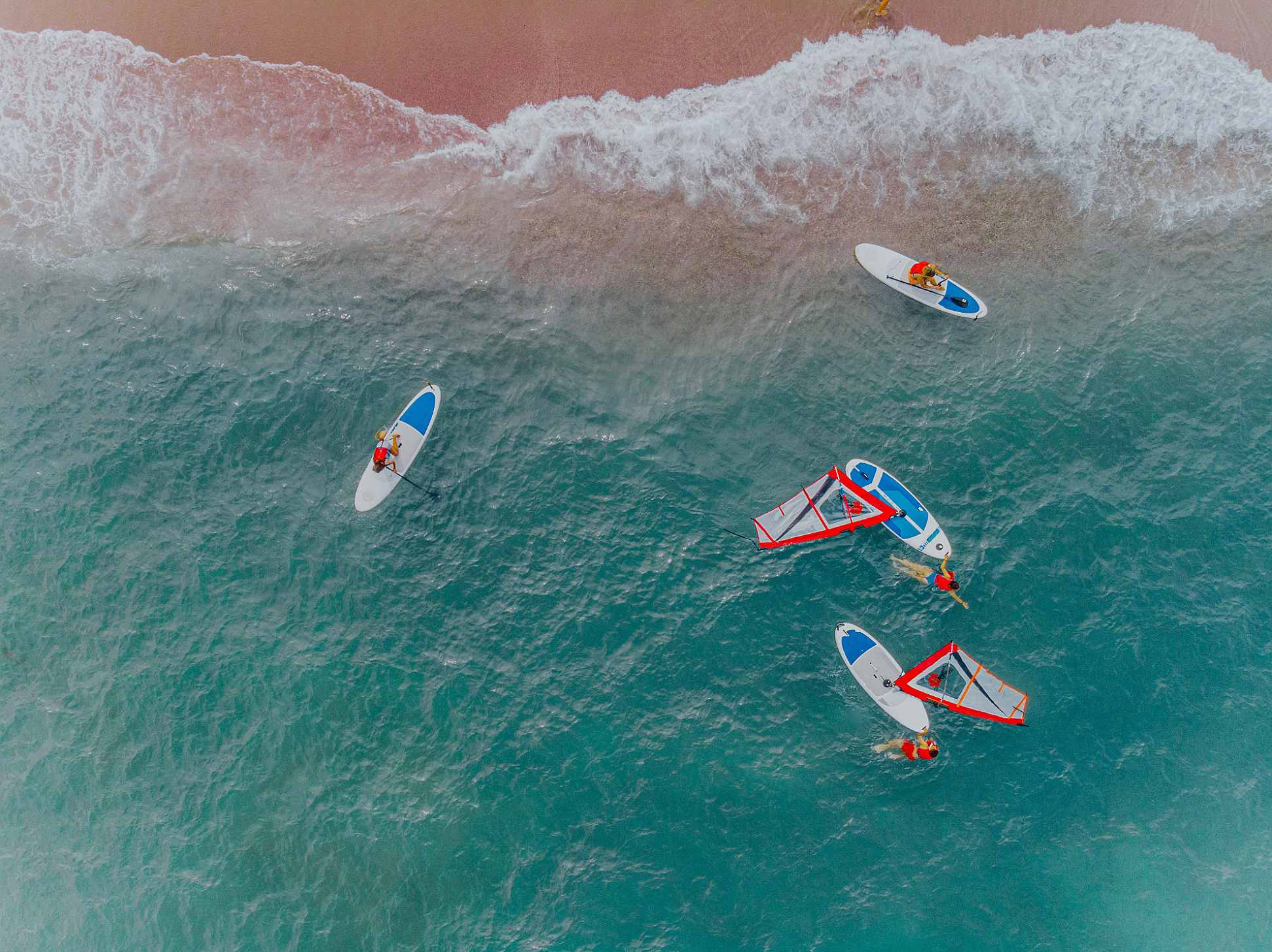 Gente en tablas de surfTaiga: Corporativa en aguas turquesas cerca de la costa de arena rosa.