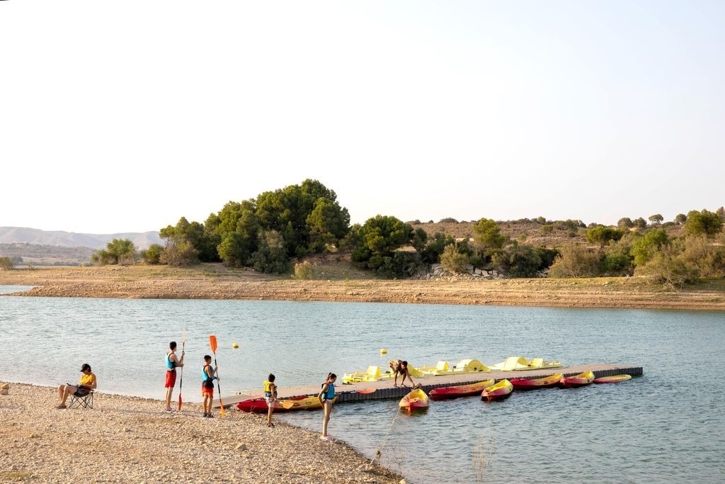 un groupe de personnes se tient au bord d' un lac avec des kayaks