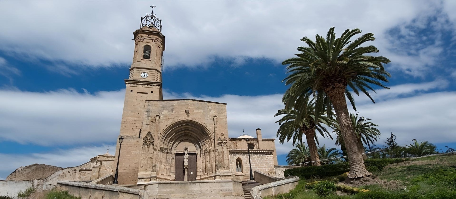 a church with a clock tower and palm trees in front of it